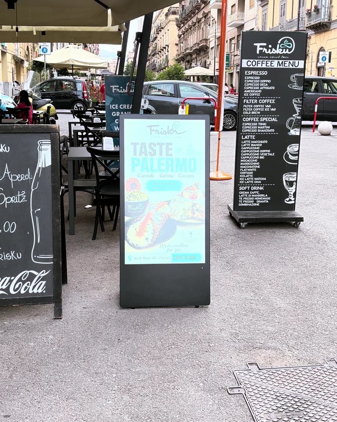 Il totem del bar acceso fra i tavoli del dehors, con una proposta gastronomica sullo schermo.