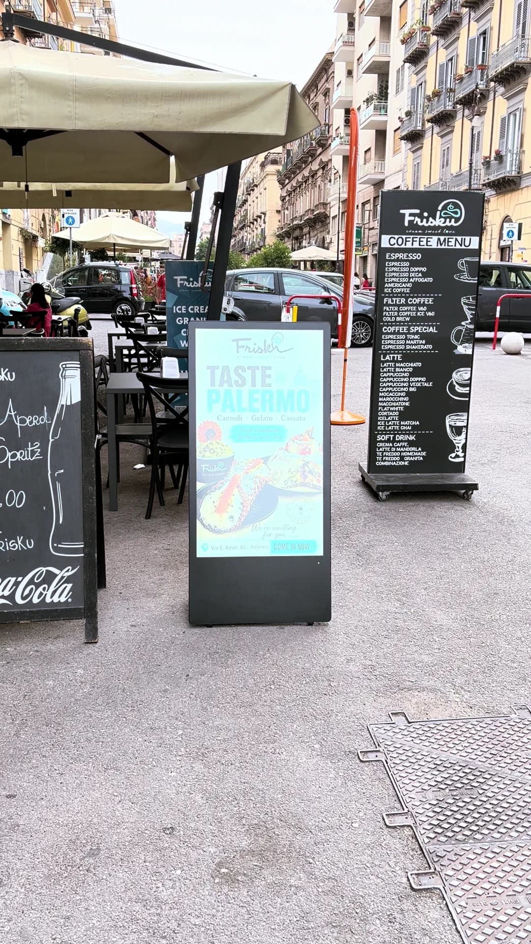 Totem digitale nel dehors di un bar con la creatività Taste Palermo, fra la lavagna dei prezzi e il menu del locale.