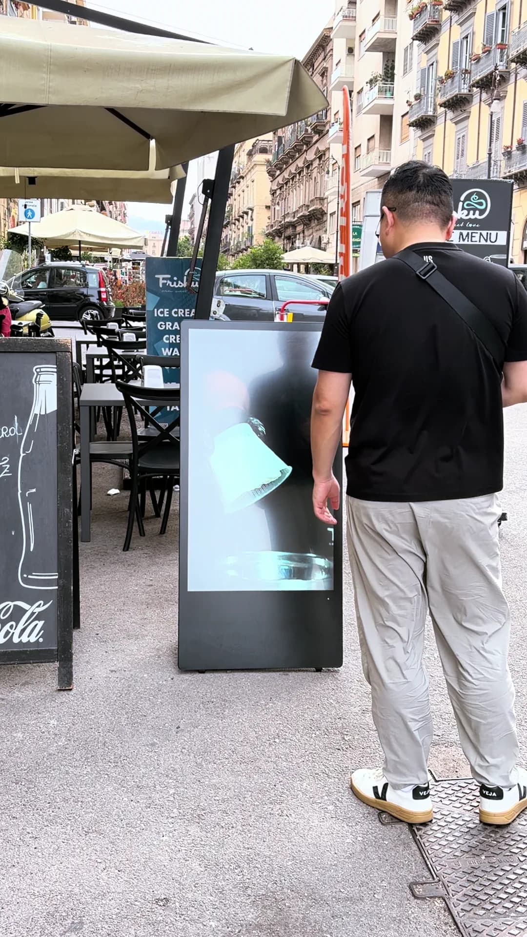 Un passante cammina accanto al totem acceso mentre sullo schermo scorre una proposta del locale.
