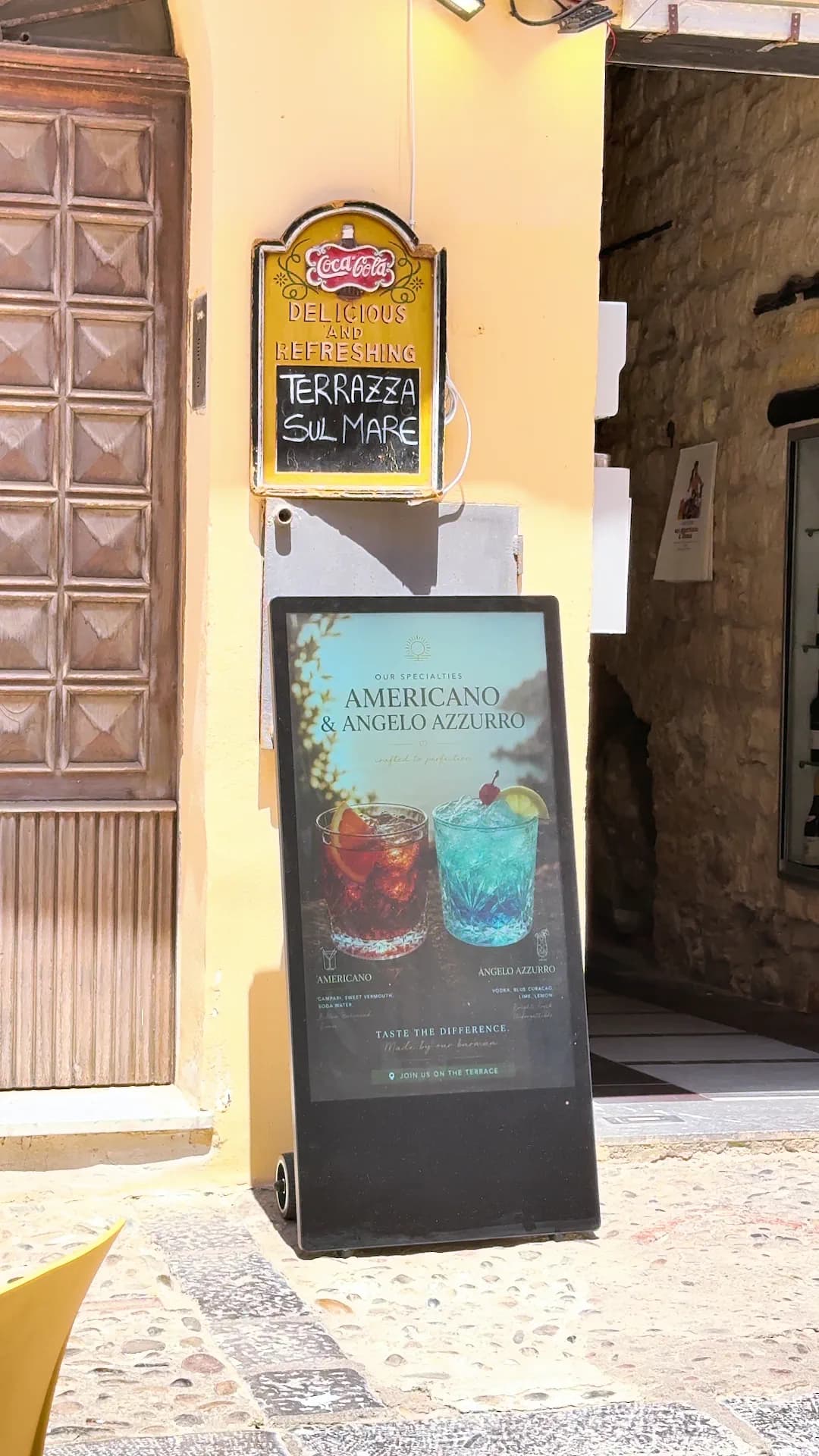 Inquadratura più ampia del totem accanto all’ingresso, con una terza creatività sullo schermo.