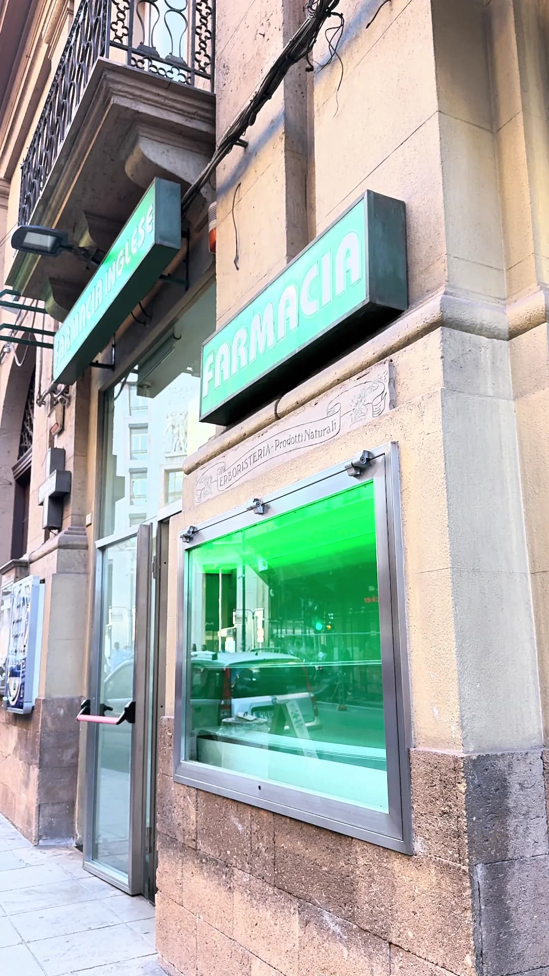 L’insegna FARMACIA e la vetrina illuminata di verde, sulla facciata in pietra.