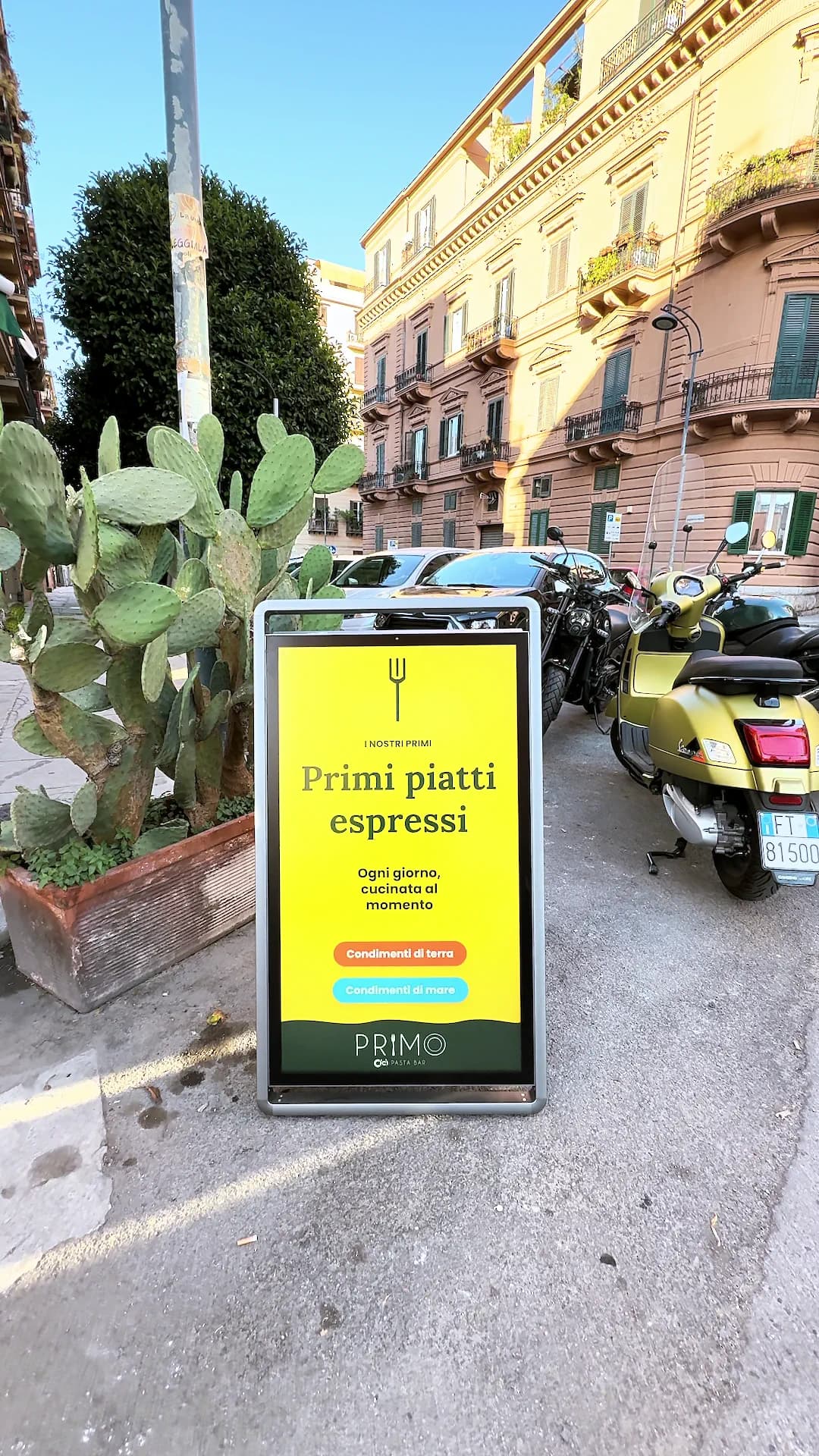 Veduta più ampia della strada con il totem acceso e il cielo sopra i palazzi.